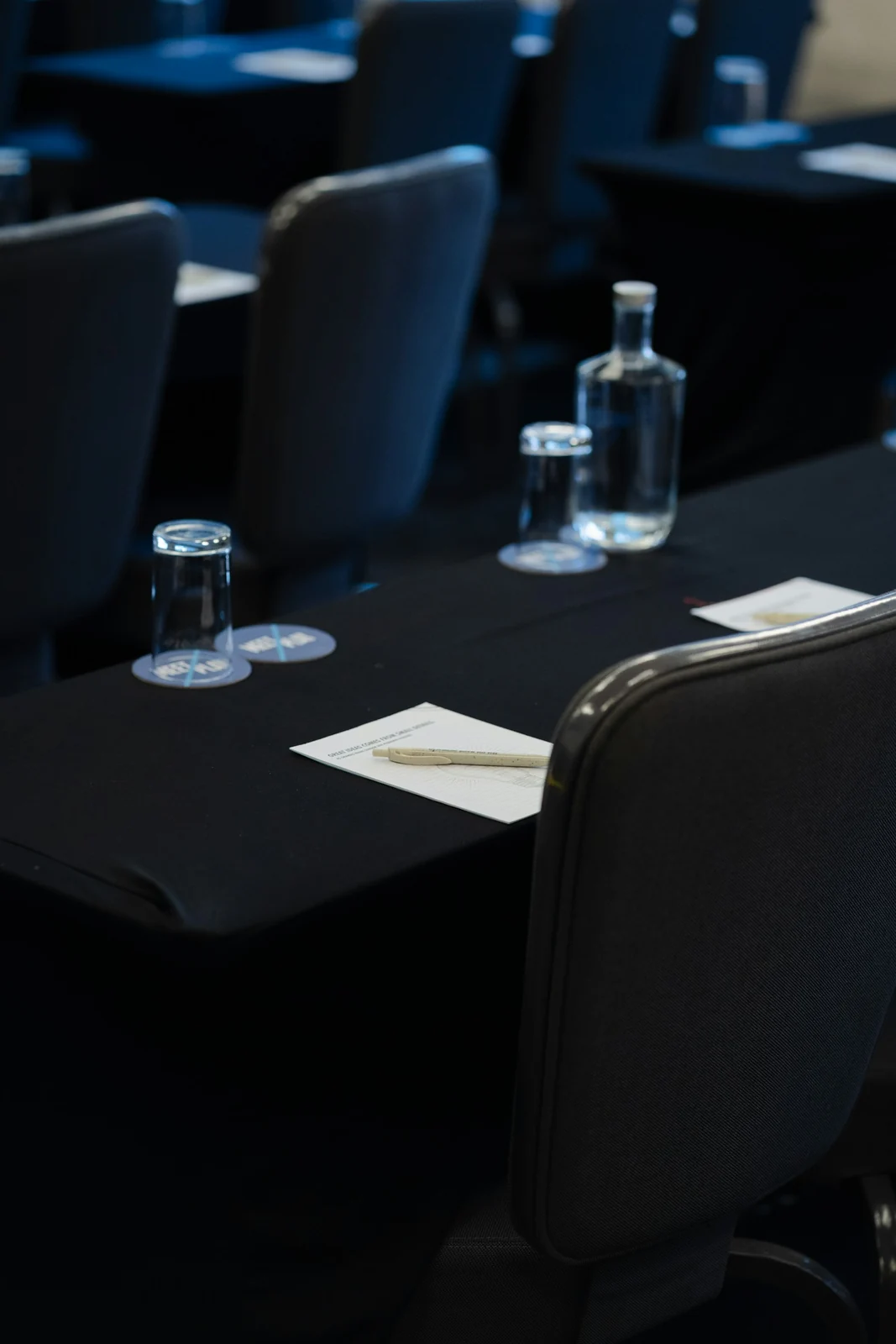 Tables de conférence préparées avec chaises, bouteilles d’eau et blocs-notes.