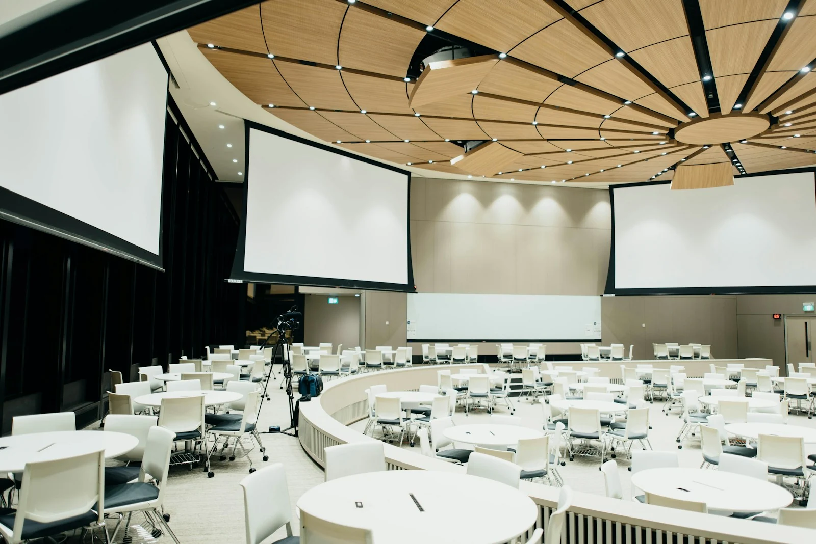 Grande salle de conférence avec tables rondes et écrans de projection.